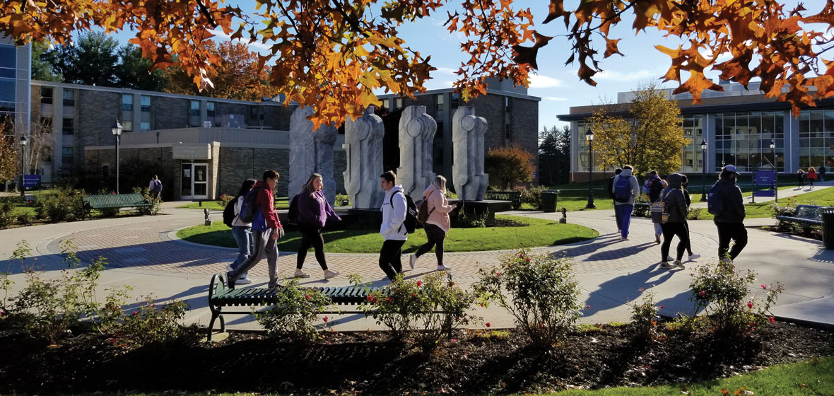 students walking on campus by the 4 sculptures in the fall