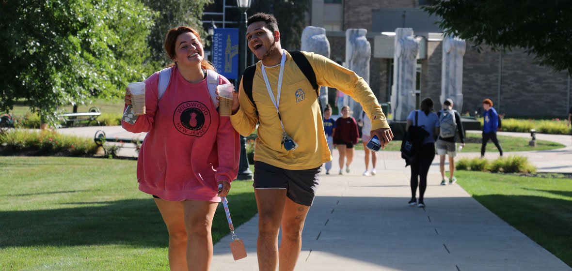 Two students smiling at us and holding iced coffees walking on campus