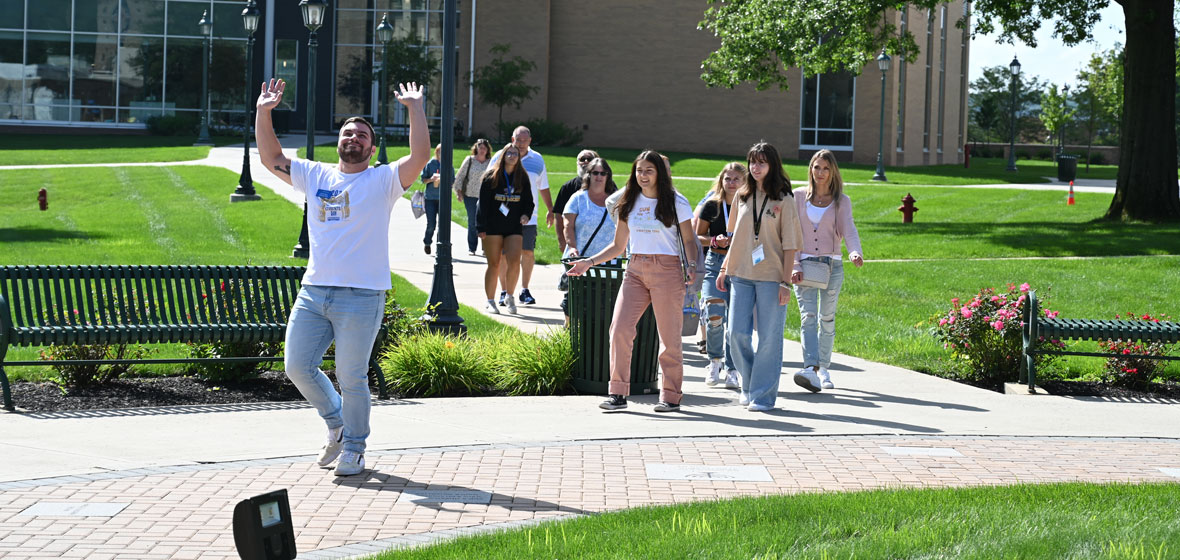 a group of students walking on campus, first students with his hands up and smiling at the camera