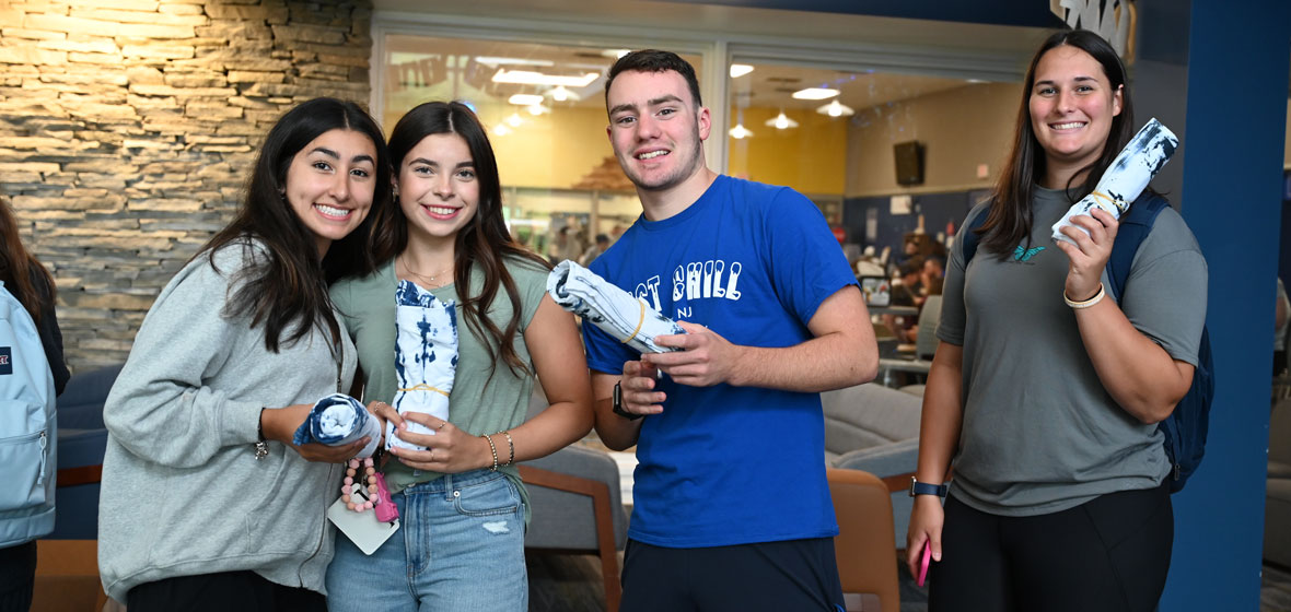 four students smiling for the camera holding rolled up tie dye t shirts