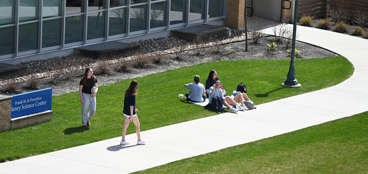 Students sitting on the lawn on campus by Henry Science Center building